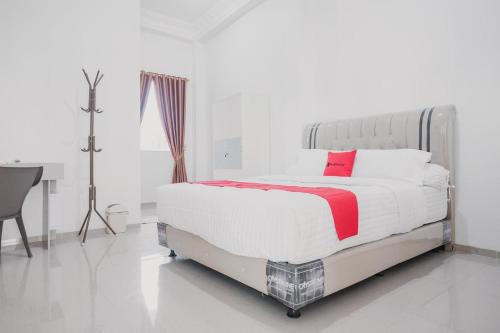 a white bedroom with a large bed with a red pillow at RedDoorz Syariah near Arafah Hospital Jambi in Jambi