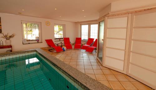 a room with a pool and red chairs and a table at Wohlfühlhotel Hörn van Diek Garni mit Schwimmbad in Bensersiel