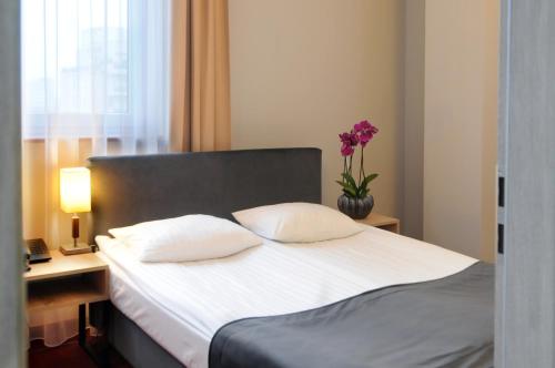a bed with two pillows and a vase with flowers at Hotel Filmar in Toruń