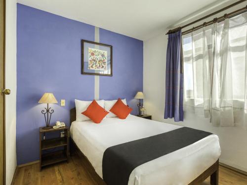 1 dormitorio con 1 cama grande y pared azul en Capital O Parador Crespo Hotel, Oaxaca en Oaxaca de Juárez