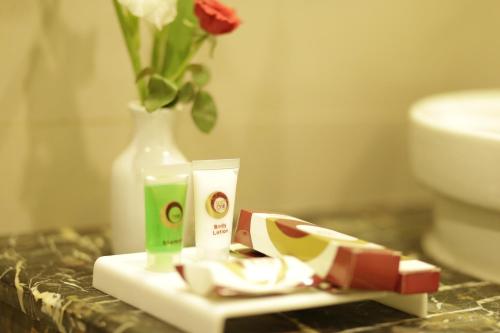 a bathroom counter with a vase of flowers and two products at Hotel One Bahawalpur in Bahawalpur