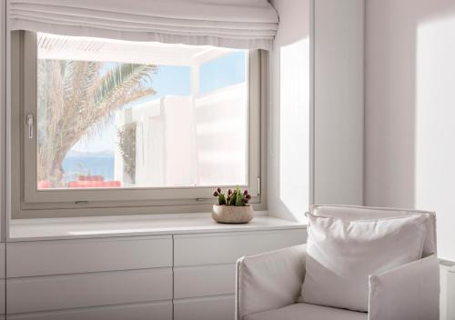 a white room with a window and a chair at O Lofos Luxury Boutique Suites in Agios Stefanos