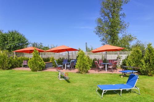 un patio con sillas, mesas y sombrillas rojas en Hof Lueck, en Esens