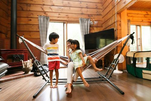two children standing on a hammock in a living room at ログハウスせせらぎ in Tsuru 