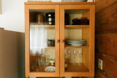 a wooden cabinet with glasses and dishes in it at ログハウスせせらぎ in Tsuru 