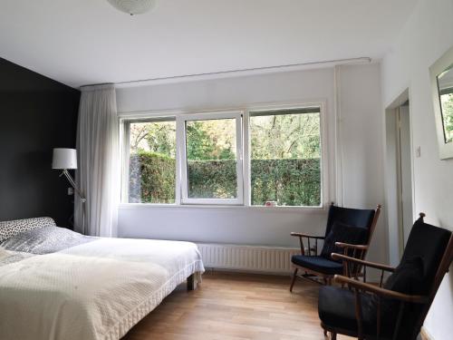 een slaapkamer met een bed en 2 stoelen voor een raam bij B & B Waalre in Waalre