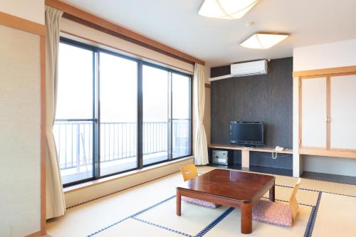 Una sala de estar con una mesa y una gran ventana. en 熱海温泉 湯の宿 平鶴, en Atami