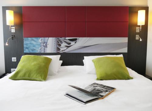 un libro en una cama con dos almohadas verdes en Mercure Honfleur, en Honfleur