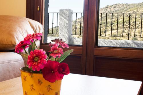 a vase with flowers on a table in front of a window at Puerta Bubión Apartamentos in Bubión