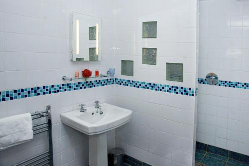 Łazienka wyposażona jest w umywalkę oraz niebiesko-białe kafelki. w obiekcie THE OLD FARMHOUSE w mieście Holmrook