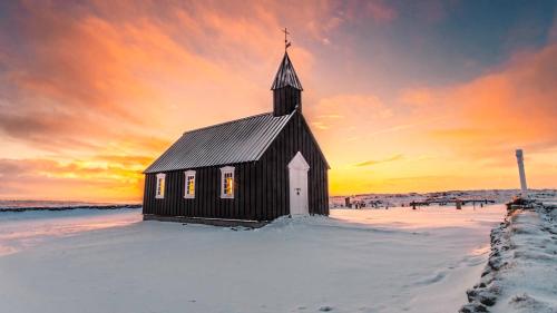 a black and white church in the snow with a sunset at Klettur in Borgarnes