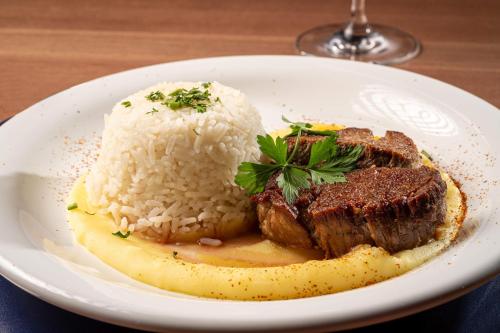 a plate of food with steak and rice on a table at Intercity Portofino Florianópolis in Florianópolis
