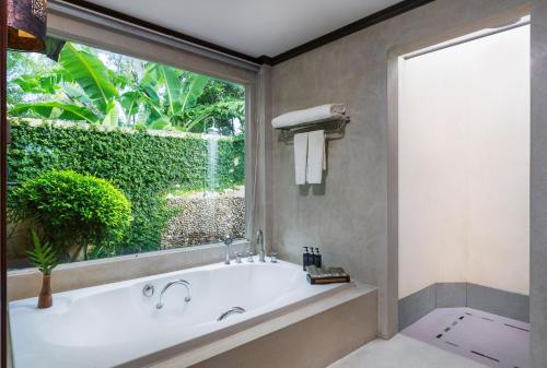a bathroom with a tub and a large window at Nora Beach Resort & Spa - SHA Extra Plus in Chaweng