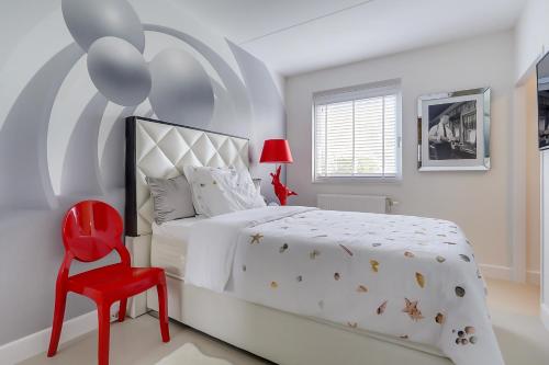 a white bedroom with a bed and a red chair at B&B Modern Times in Amsterdam