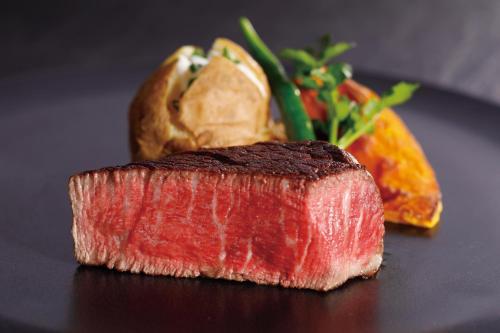 a piece of meat on a black plate with vegetables at Hotel New Otani Tokyo Garden Tower in Tokyo