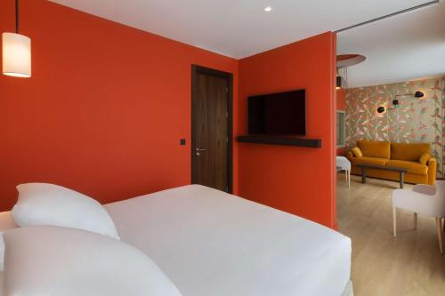 a bedroom with a white bed with an orange wall at Hotel L'Arbre Voyageur - LILLE in Lille