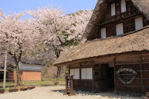a building with a thatch roof withakura trees in the background at Gokayama Onsen Akaokan in Nanto