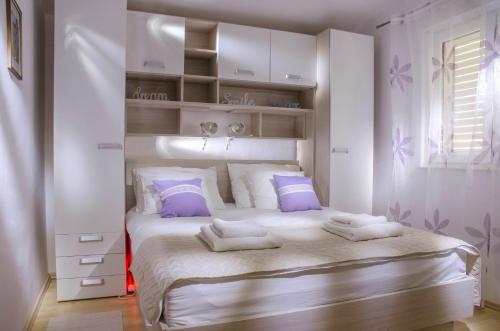 a white bedroom with a large bed with purple pillows at Apartments IDa II in Baška