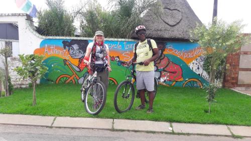 two men standing next to a bike in front of a wall at Authentic Bicycle Tours and Backpackers in Soweto