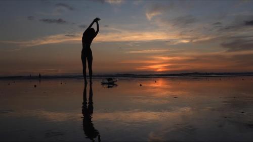 a statue of a woman standing on the beach at sunset at Ride On! Surf Hotel in Nosara