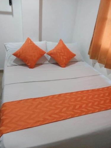 Una cama con dos almohadas naranjas encima. en Hotel Torres del Parque No1, en Soledad