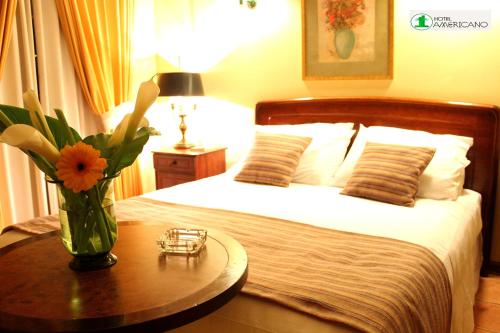 1 dormitorio con 1 cama con un jarrón de flores sobre una mesa en Hotel Americano, en Arica