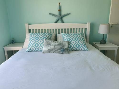 1 cama blanca con almohadas y una cruz en la pared en Sea and Mountain View Apartment, en Gordonʼs Bay