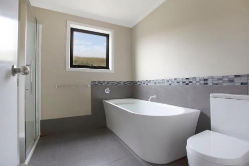 een badkamer met een bad, een toilet en een raam bij Otway coastal villas in Princetown