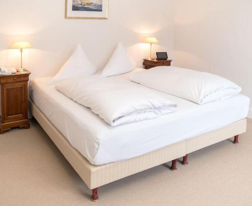 a large bed with white sheets and pillows at Strandhotel Strande in Strande