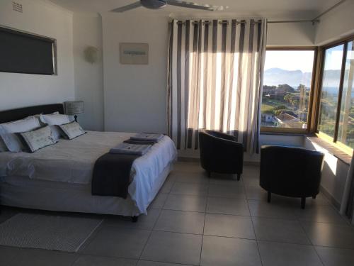 a bedroom with a bed and two chairs and a large window at Dream a Little in Simonʼs Town