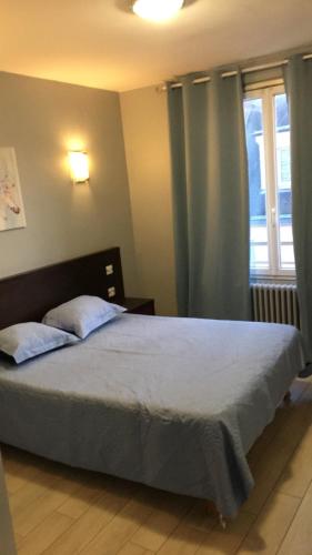 a bedroom with a bed with blue curtains and a window at Hotel Les Arcades in Rouen