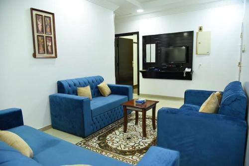 sala de estar con 2 sillas azules y TV en شقق جنان المفروشة Jenaan Apartments en Najrán