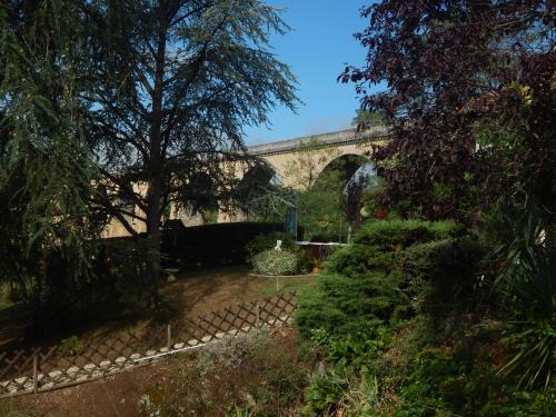 a bridge over a garden with trees and bushes at The Petite Chalet Chambre d'hôtes in LʼIsle-Jourdain