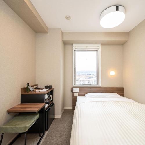 a room with a bed and a desk and a window at Super Hotel Joetsu Myoko-Eki Nishiguchi in Joetsu