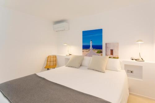 a bedroom with a white bed with a picture of a lighthouse at Apartamentos Roca Plana in Es Pujols