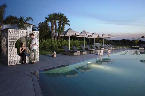 a man and a woman standing next to a swimming pool at Lagouvardos Village Hotel in Marathopoli
