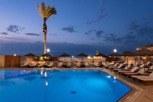 a pool with lounge chairs and a palm tree at night at Blue Sky City Beach Hotel in Rhodes Town