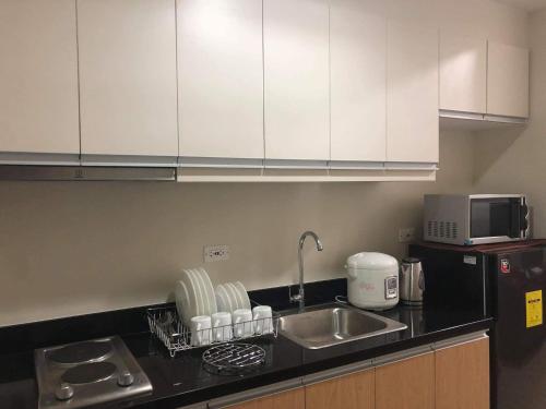 eine Küche mit weißen Schränken, einer Spüle und einer Mikrowelle in der Unterkunft One Madison Place, Tower 2 - 10N MEGAWORLD Iloilo in Iloilo City