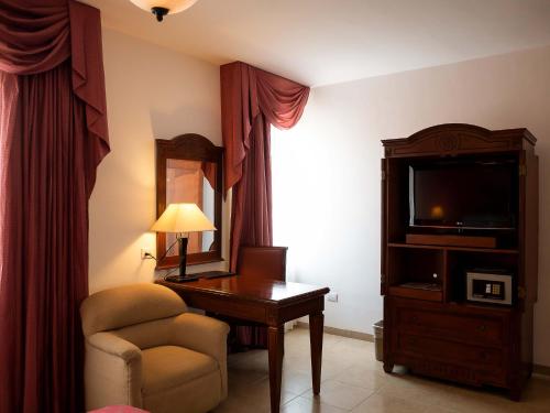Habitación de hotel con escritorio, silla y TV. en Hotel Hacienda Real, en Ciudad del Carmen