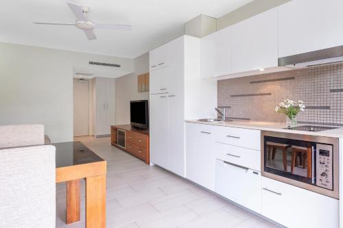 a white kitchen with white cabinets and a tv at Drift Palm Cove in Palm Cove
