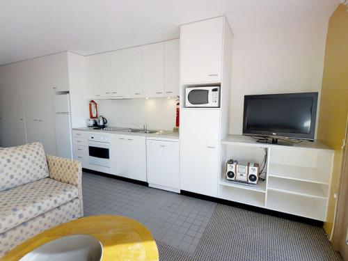 a small kitchen with white cabinets and a television at Studio 2 - The Stables Perisher in Perisher Valley