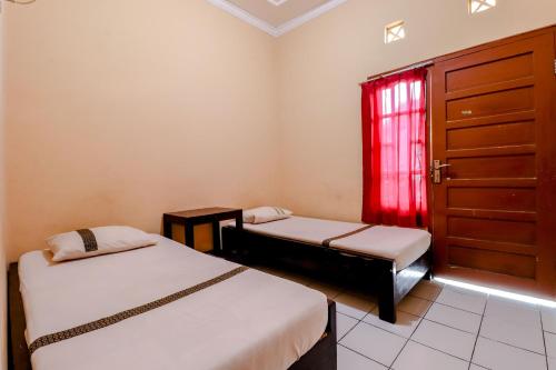a room with two beds and a window with red curtains at Griya Barokah in Kalasan