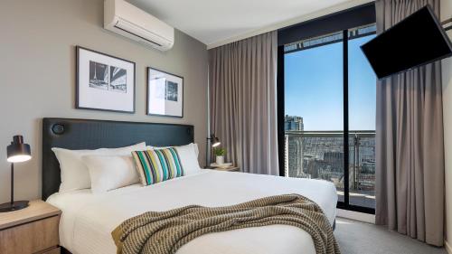 a bedroom with a bed and a large window at Oaks Melbourne on William Suites in Melbourne