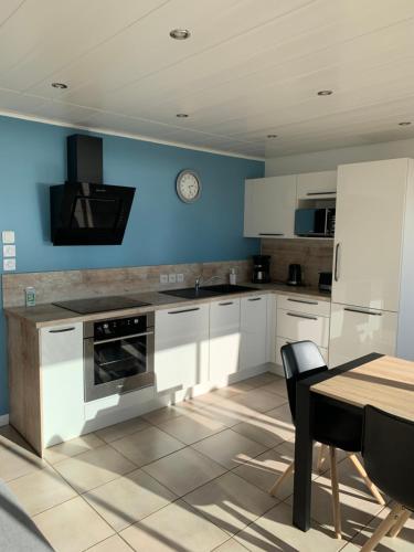 une cuisine avec des placards blancs, une table et une horloge dans l'établissement Le Face Mer - La Baule, à La Baule