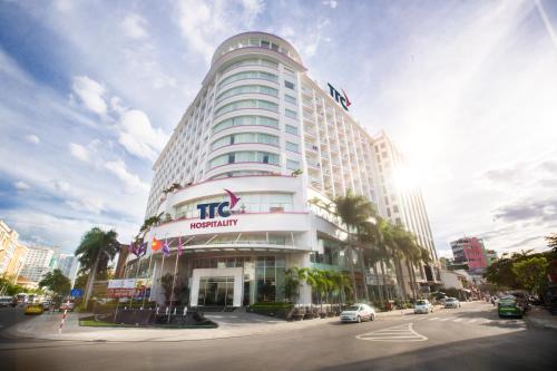 un grand bâtiment blanc dans une rue de la ville avec des voitures dans l'établissement TTC Hotel - Michelia, à Nha Trang