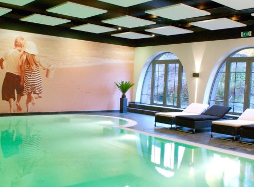 a swimming pool with two chairs and a painting on the wall at Parkhotel Horst - Venlo in Horst