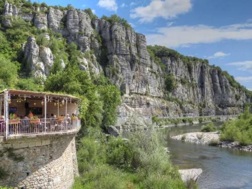 a restaurant on a bridge over a river next to a mountain at Vogüé Meublé 2 étoiles, Un écrin de beauté et de nature in Vogüé