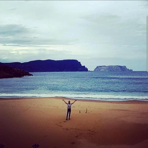 a person standing on a beach with their arms outstretched at Ruby's Cottage Farm Stay in Port Arthur