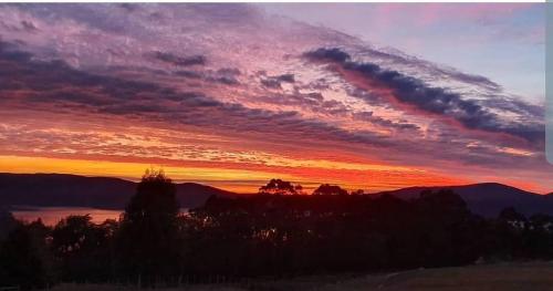 a sunset over the mountains and a lake at Ruby's Cottage Farm Stay in Port Arthur