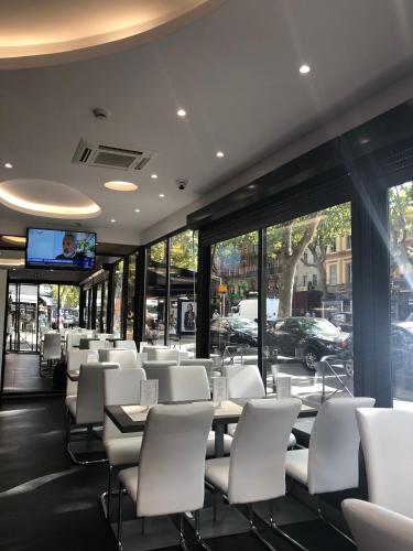Un comedor con sillas y mesas blancas y ventanas. en Hotel Victor Hugo, en Toulouse